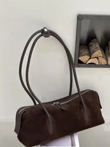 Dark brown suede bag hanging against a light wall, with long leather handles and a silver zipper