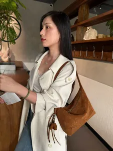 Side view of a woman carrying a brown suede-textured shoulder bag with a zipper and tassel