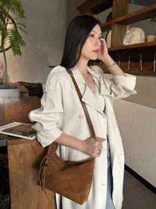 Woman wearing a brown suede shoulder bag with a slim leather strap and drawstring charm indoors
