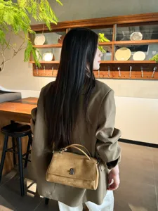 Back view of a woman carrying a tan suede shoulder bag with a curved handle and metal clasp