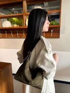 Side view of a model wearing an olive suede-textured shoulder bag with dark leather trim indoors