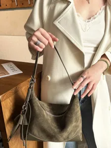 Close-up of an olive gray suede-textured shoulder bag with silver hardware, shown being carried