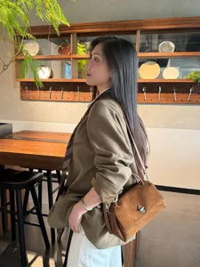Side view of a model carrying a brown suede-textured bag with a metal clasp in a warm wood interior