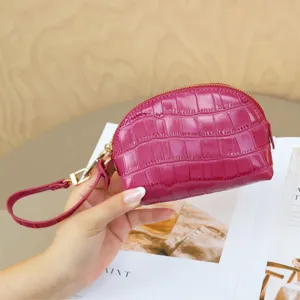 Close-up of a fuchsia crocodile-embossed pouch with gold zipper and wrist strap, held in hand