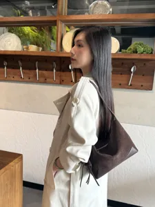 Side view of a model carrying a dark brown suede shoulder bag with leather trim and a zip top