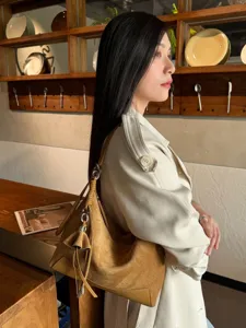 Side view of a model wearing a caramel suede-textured shoulder bag with silver chain accents
