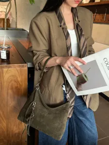 Olivgrüne Veloursledertasche mit silbernem Kettenanhänger, über der Schulter im Café getragen