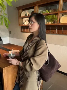Frau mit dunkelbrauner Veloursledertasche, silbernen Beschlägen und Quaste an einer Cafétheke