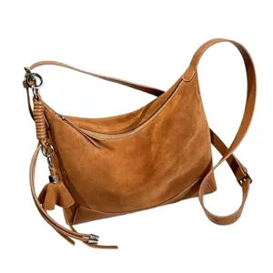 Brown suede crescent shoulder bag with adjustable strap, zip top and tassel, shown at an angle