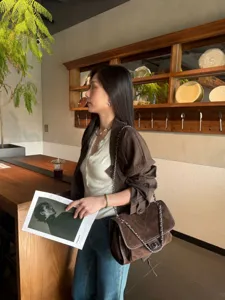 Vista lateral de una mujer con bolso de ante acolchado marrón oscuro y cadena plateada en una cafetería