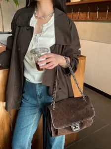 Bolso marrón de ante acolchado llevado en una cafetería, con cadena plateada y cierre giratorio