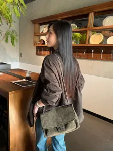 Una mujer lleva un bolso de ante acolchado con cadena junto a la barra de madera de una cafetería