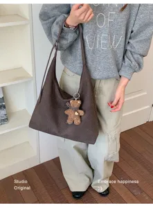 Une personne porte un cabas tissé brun foncé avec un pendentif ourson, sur une tenue décontractée.