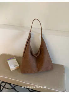 Sac brun à texture tressée, avec longue bandoulière et boucles argentées, posé sur un banc beige