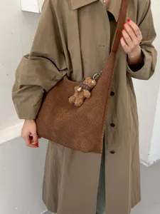 Grand cabas d'épaule brun spacieux, à texture tressée avec breloque ourson, porté avec un manteau