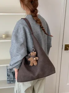 Grand cabas tressé brun foncé porté à l’épaule, avec un petit pendentif ourson décoratif