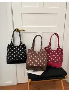 Drie fluwelen shoppers met stippen in zwart, bruin en bordeaux staan naast een witte deur