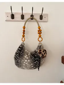 Borsa in ecopelliccia grigia maculata, appesa al muro con manico in perline e ciondolo leopardato