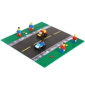 Building block road play mat with green studded base, yellow lane markings, figures and toy cars