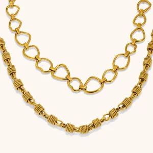 Close-up of two layered gold-tone necklaces with open links and textured cylindrical accents