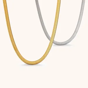 Close-up of layered flat snake chains in gold and silver on a warm ivory backdrop
