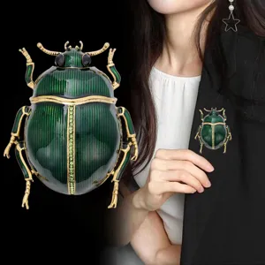 Close-up of green enamel beetle with gold-tone legs and jeweled center, shown on a black blazer