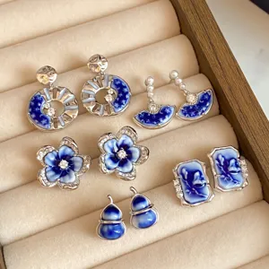 Assorted blue-and-white enamel earrings with silver-tone settings arranged on a beige velvet tray
