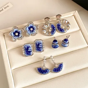 Blue-and-white enamel earrings in floral, geometric and pearl-accented styles in a cream jewelry box