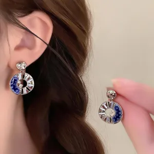 Close-up of blue and white enamel drop earrings with sparkling accents, worn and held by hand