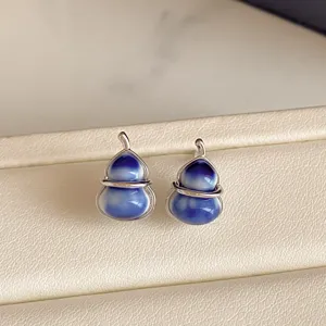 Close-up of blue-white glazed gourd earrings with silver-tone wire settings on a beige tray
