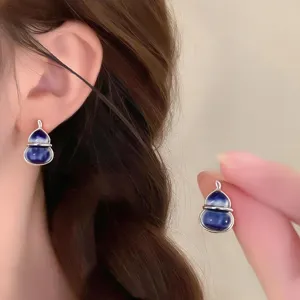 Close-up of blue-and-white glazed gourd earrings with silver frames, shown worn and held by hand