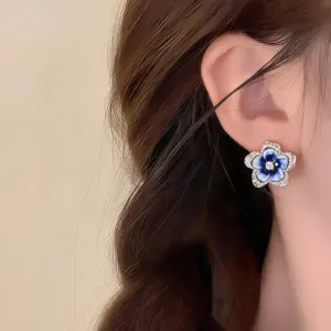 Close-up of a blue enamel flower earring with a sparkling center, worn against dark brown hair