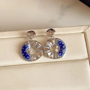 Paired silver-tone earrings with blue floral enamel, openwork spokes and sparkling centers
