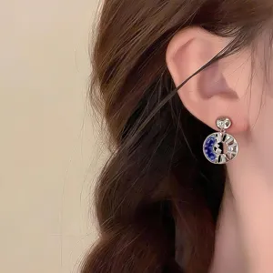 Close-up of a circular silver earring with blue inlay, openwork and sparkling accents, worn on ear