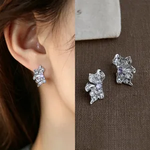 Close-up of a silver floral stud with purple center stones and clear accents, worn and displayed