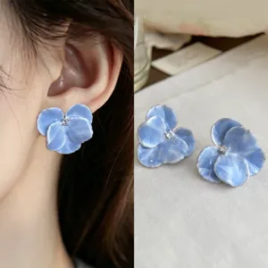 Close-up of blue glossy flower earrings with a clear center stone, shown worn and laid flat