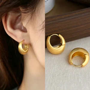 Close-up of brushed matte gold crescent hoop earrings, worn and displayed on linen beside wood