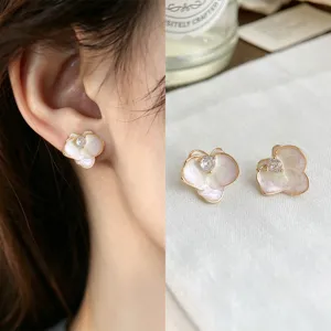 Close-up of pale pink enamel flower studs with gold-tone edges and clear stones, worn and displayed