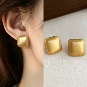 Close-up of square matte gold stud earrings, shown worn and displayed on natural linen fabric