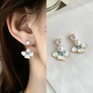 Close-up of blue and white enamel flower earrings with heart-shaped stones and pearl accents