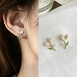 Close-up of pearl-like flower petals, green enamel leaves and gold-tone details on the earrings