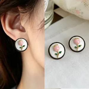 Close-up of pink tulip studs with green leaves, set on white discs with black and gold rims