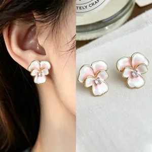 Close-up of pink and white enamel flower earrings with gold-tone edges and crystal centers