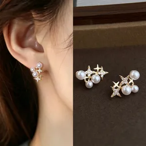 Close-up of a gold star-and-pearl earring worn on an ear, with its pair displayed on velvet