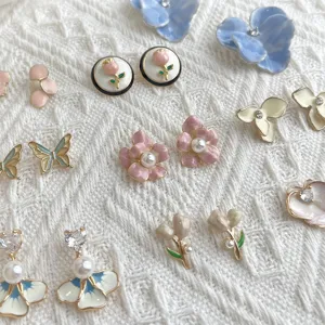Assorted enamel flower, butterfly and pearl earrings arranged on textured white fabric