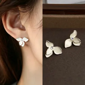 Close-up of white enamel flower earrings with gold edges and clear stones, worn and shown as a pair