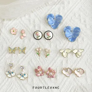 Assorted colorful earrings on white knit fabric, featuring flower, butterfly and heart designs