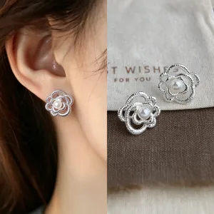 Close-up of silver openwork camellia stud earrings with layered petals and pearl-like centers