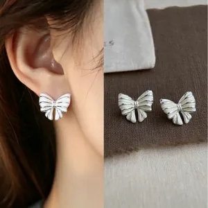 Close-up of a silver-tone pleated bow stud worn on the ear, with its pair displayed on linen.