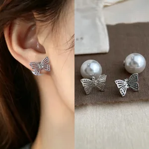 Close-up of an openwork silver butterfly earring worn on the ear, with pearl backs beside it
